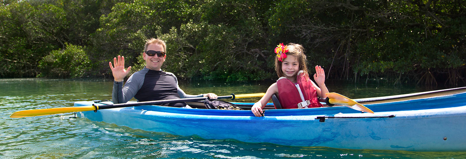 Adult and child waving from a kayak, suggesting a recreational activity enjoyed by those houseboat rentals nearby.