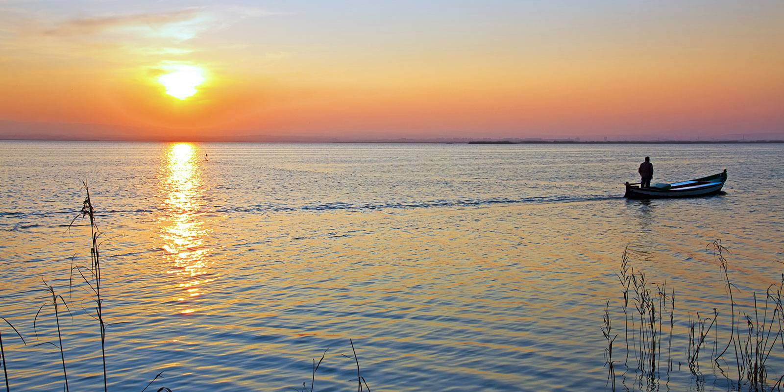 A tranquil sunset over water with a small boat, suggesting the peaceful surroundings of marina potential houseboat rentals.