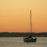 A sailboat anchored on calm water at sunset, a visual contrast when considering can houseboats sail.