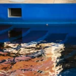 The deep blue interior of a swimming pool with visible steps, subtly reflecting surrounding colors, alluding to the corrosive environment of saltwater and how does saltwater affect boat paint.
