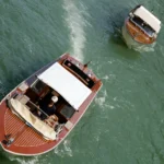 An overhead view of a classic wooden boat with a white cabin moving on water, and another boat nearby, illustrating a vessel that clearly answers the question, Do houseboats have engines?